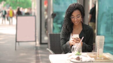 Eine Frau sitzt im Außenbereich eines Gastronomiebetriebs an ihrem Smartphone