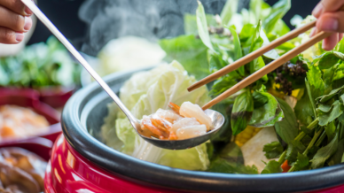 Garnelen in einem Löffel werden mit Stäbchen in den Hot Pot gelegt.