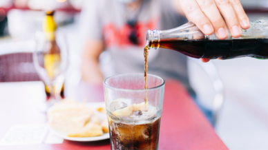 Cola wird aus einer Flasche in ein Glas mit Zitrone geschüttet