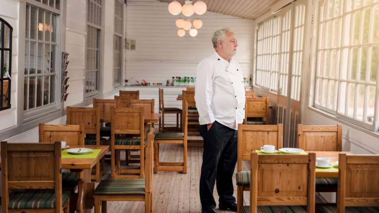 Koch steht in leerem Restaurant und blickt aus dem Fenster