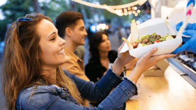 Lächelnde Frau nimmt Essen von einem Food Truck entgegen