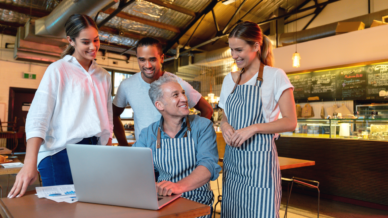 Servicekräfte stehen hinter ihrem Chef, der am Laptop sitzt in einem Restaurant